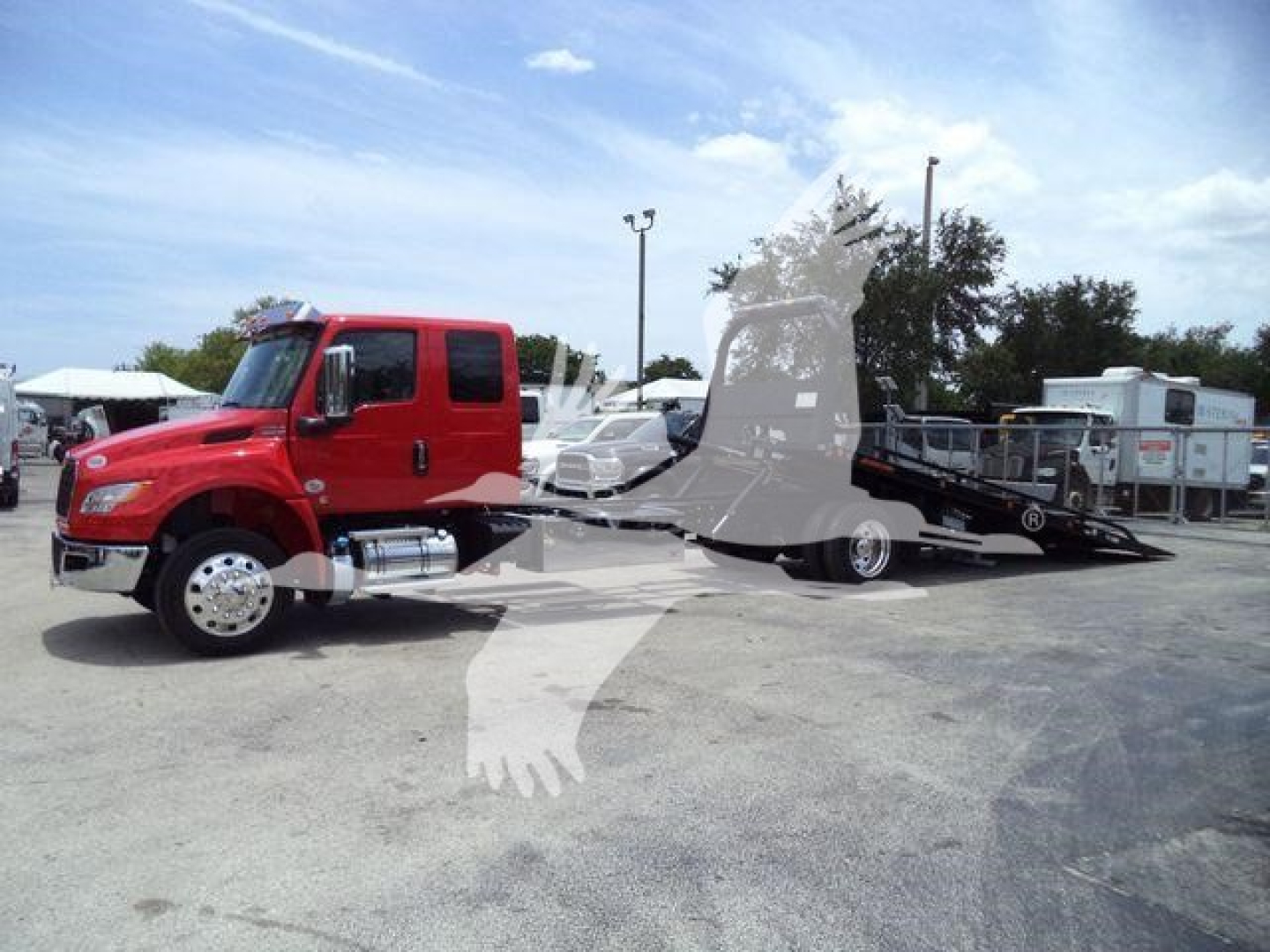Red International MV rollback tow truck with a long flatbed trailer in a dealership lot, side view showing cab and chassis.
