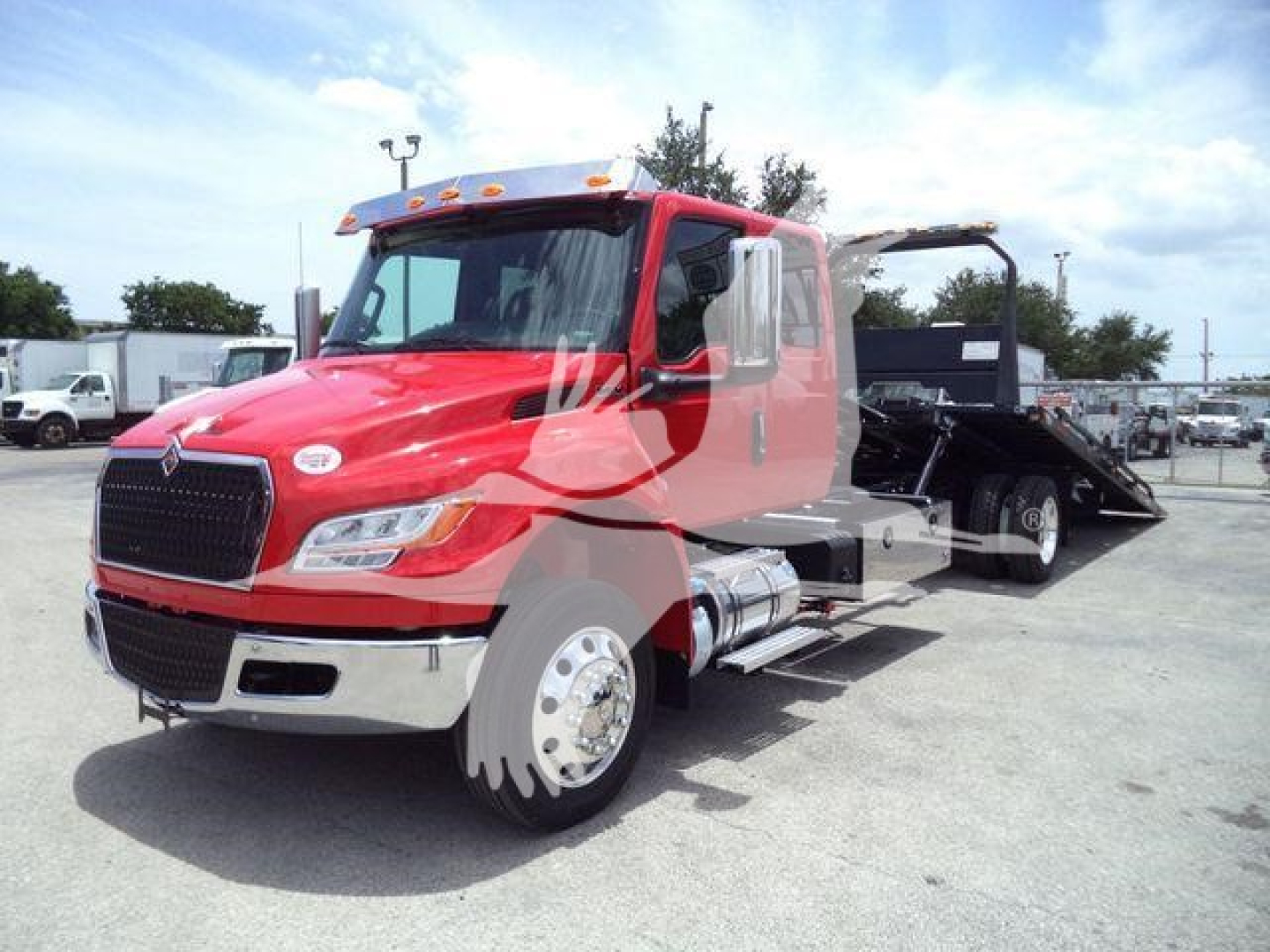 Tow truck on a dealership lot showing a red International truck cab and a flatbed rollback.