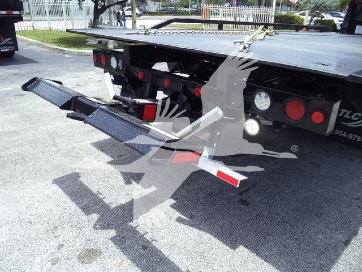 Trailer rear showing fold-down ramps and taillights on a rollback, with steel platform and trailer markings visible.