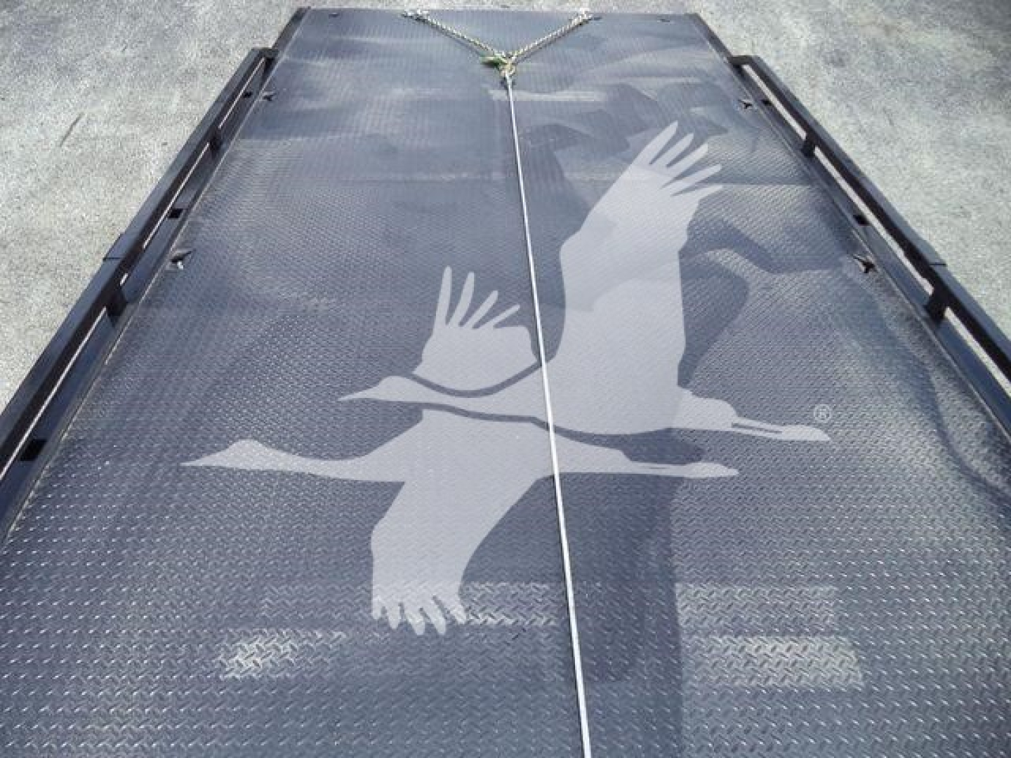 Truck bed or loading platform with a large white bird graphic, likely a crane, on a diamond plate surface; rope and anchors at top center.