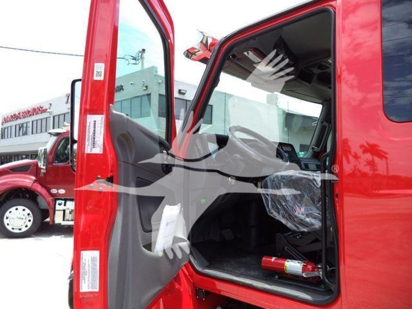 Truck cab interior with door open, red exterior, seating area, gear shifter, dashboard, and a fire extinguisher on the floor; appears to be a new International MV rollback truck.