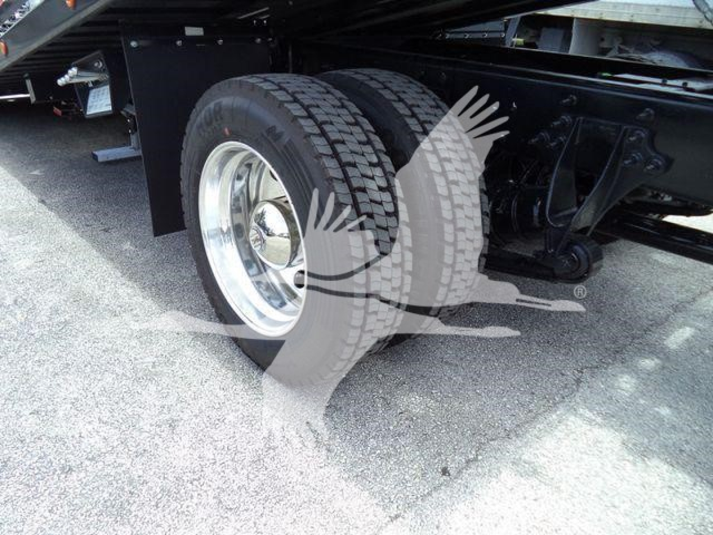 Truck wheel and dual rear tires on a rollback chassis showing chrome rims and suspension components.