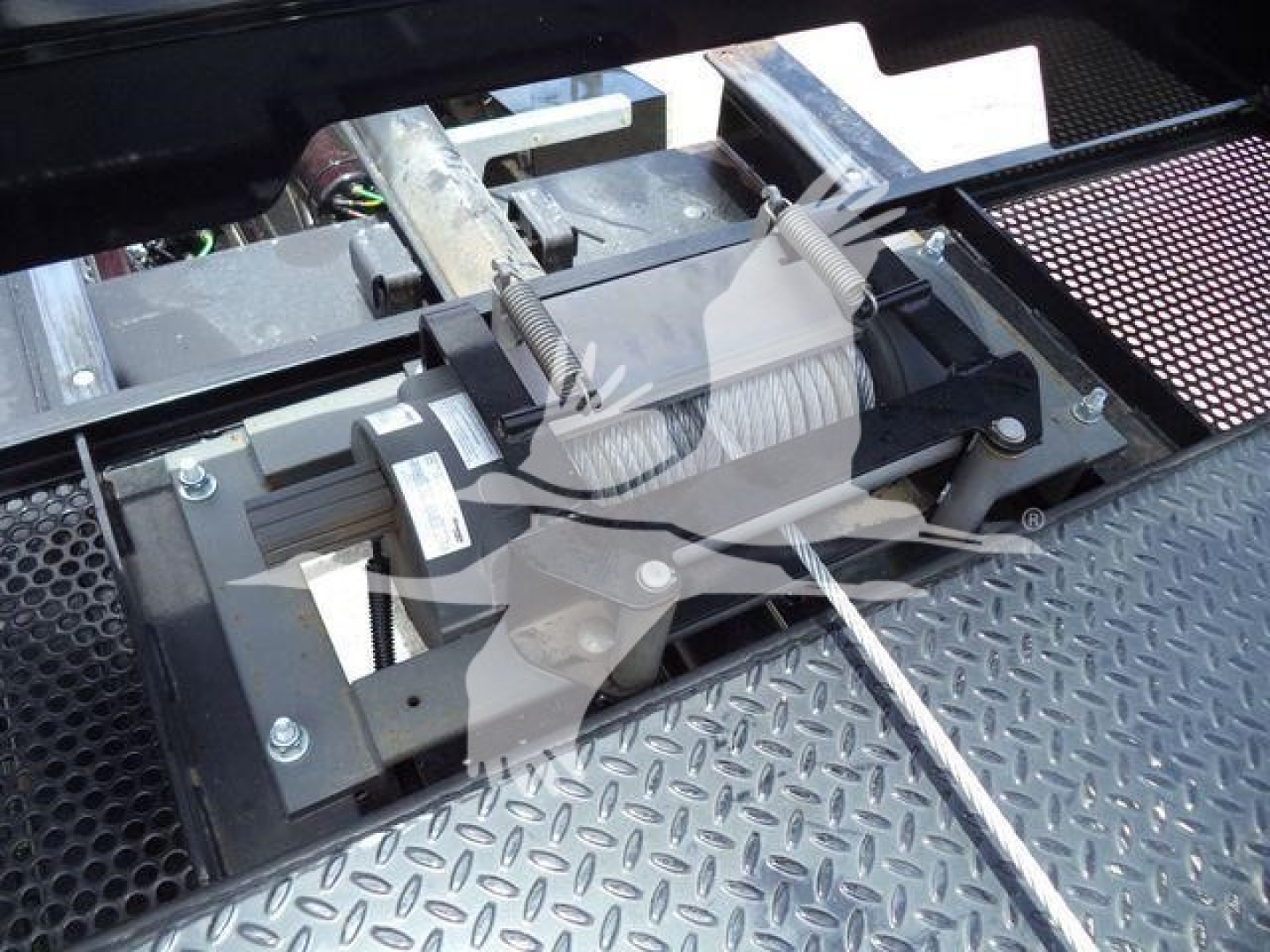 Truncated view of winch/boom assembly on a rollback tow truck with cables and rollers visible on diamond plate surface.