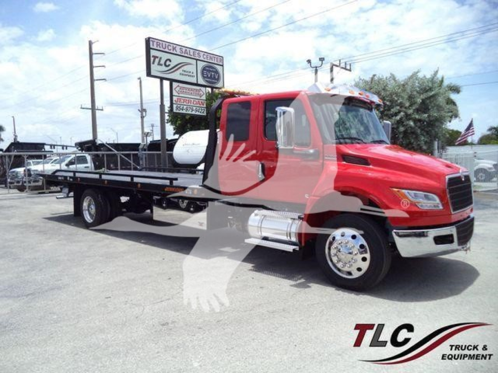 International MV tow truck on dealership lot showing red cab and rollback bed with TLC logo watermark.