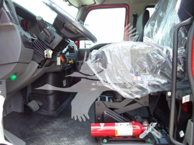 Cab interior of a new International MV truck showing driver seat wrapped in plastic and a red fire extinguisher on the floor, steering wheel, pedals, and dashboard visible.