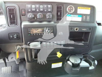 Dashboard and controls of an International MV truck cab showing ignition, steering area, climate controls, cup holders, and a yellow key, with warning stickers visible.