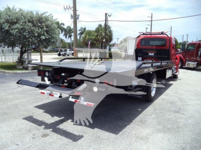 Flatbed tow truck rear view showing rollback bed and equipment, International MV likely chassis, red cab in background.