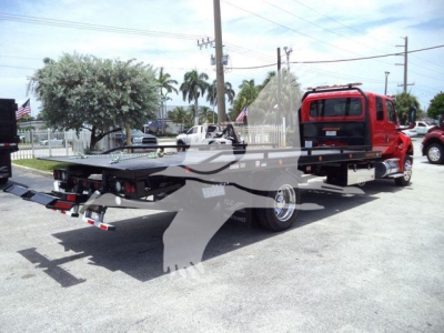 Flatbed tow truck with red cab and black bed, rollback equipment, in a dealership lot.