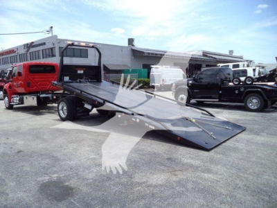 Truck bed with a tilted flatbed car hauler on a dealership lot, International MV not visible; multiple trucks in background