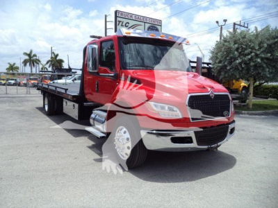 Truck showing a red International MV rollback wrecker with flatbed in a dealership lot, front grille, chrome bumper, and tow truck equipment visible.