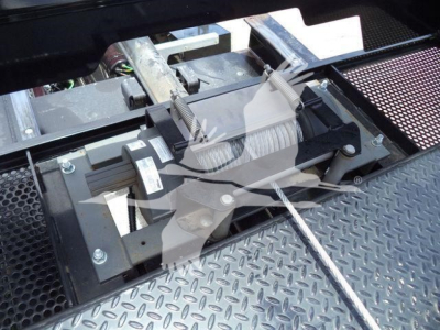 Truncated view of winch/boom assembly on a rollback tow truck with cables and rollers visible on diamond plate surface.