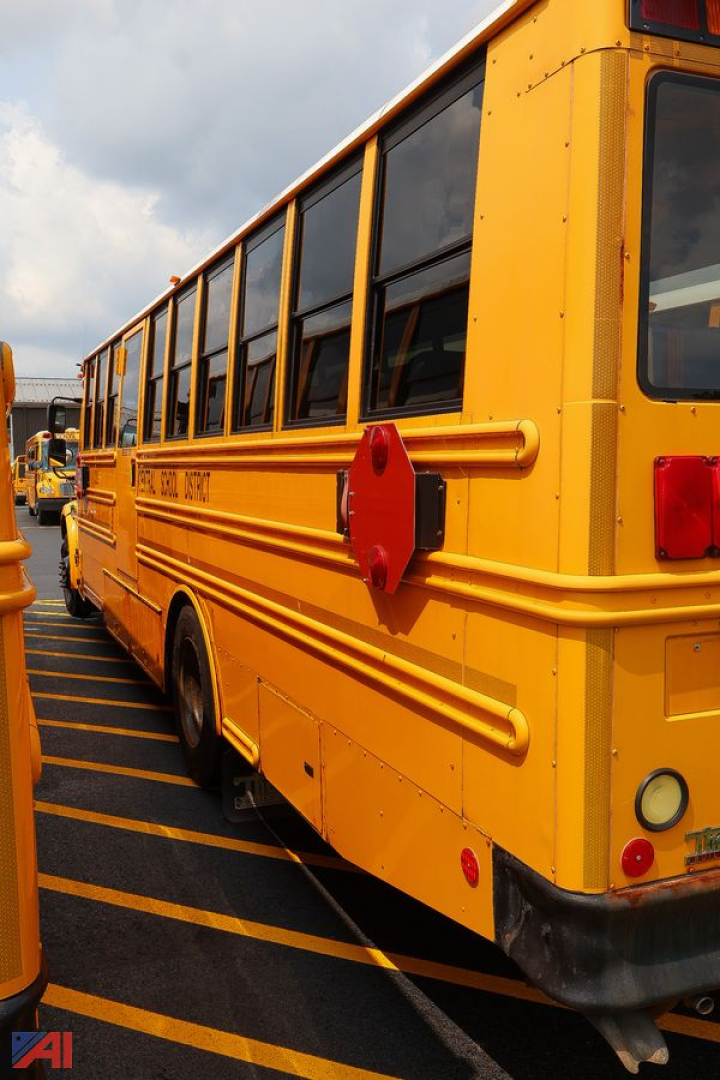 School bus side view showing bright yellow body, black trim, and red reflective stop sign mounted on the side near rear window.
