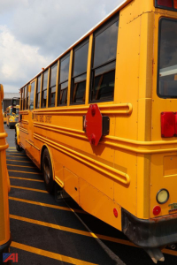 School bus side view showing bright yellow body, black trim, and red reflective stop sign mounted on the side near rear window.