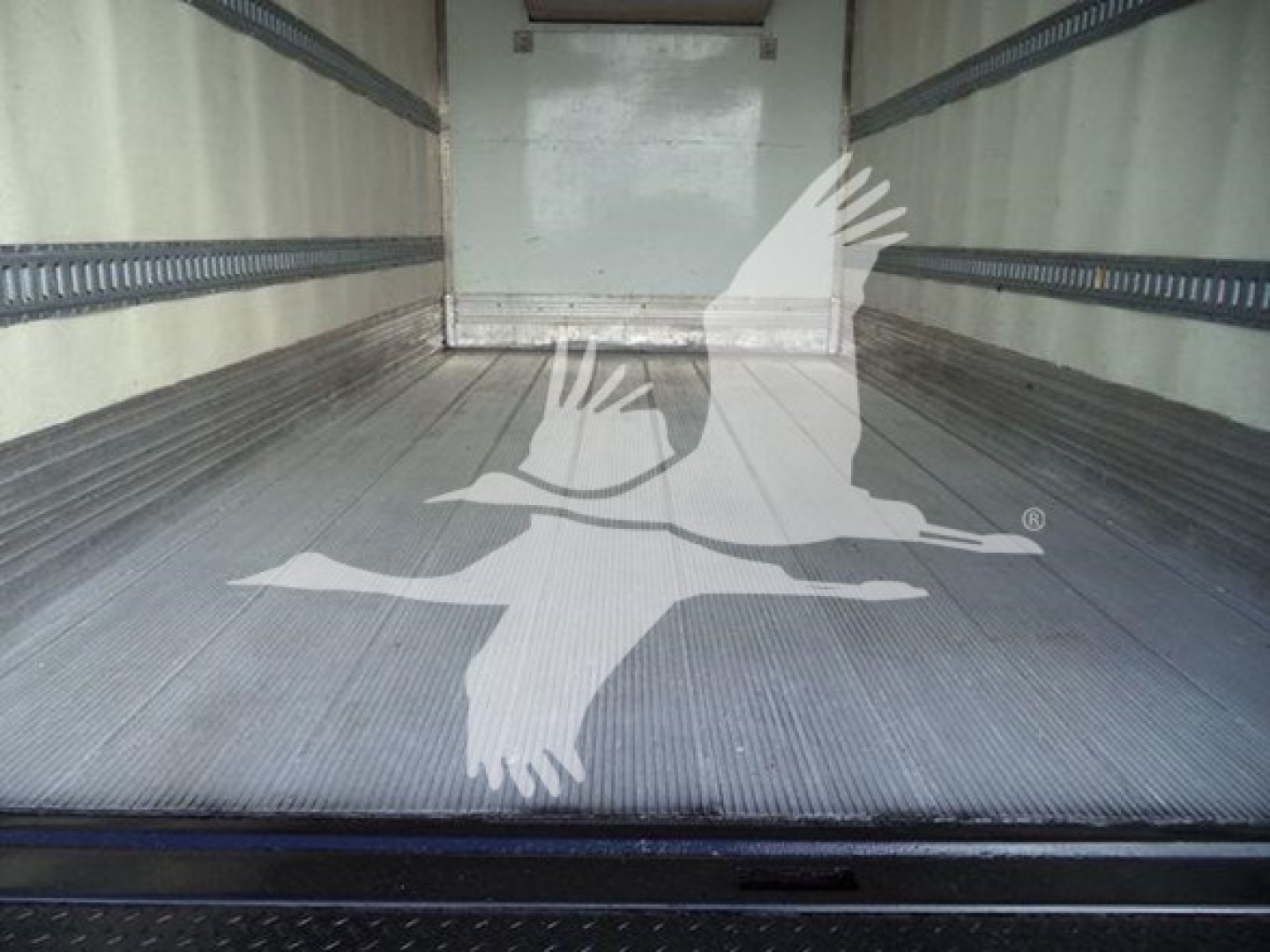 Truck trailer interior showing aluminum ribbed floor and rear door threshold.