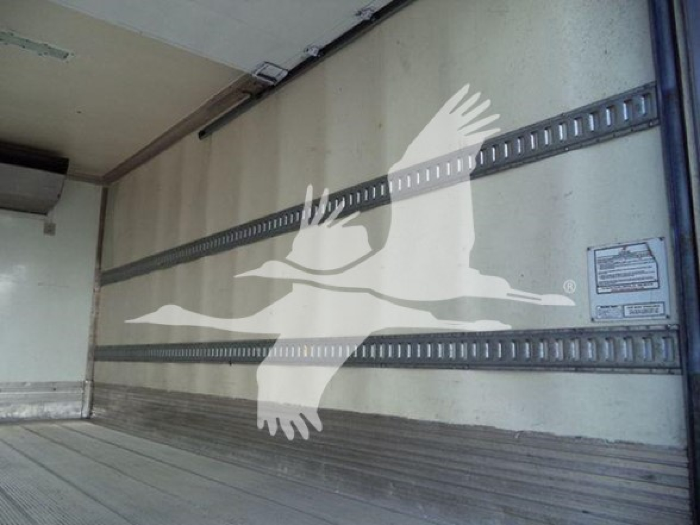 Truck trailer interior with metal rails and a watermark of a flying bird/logo overlaying the wall.