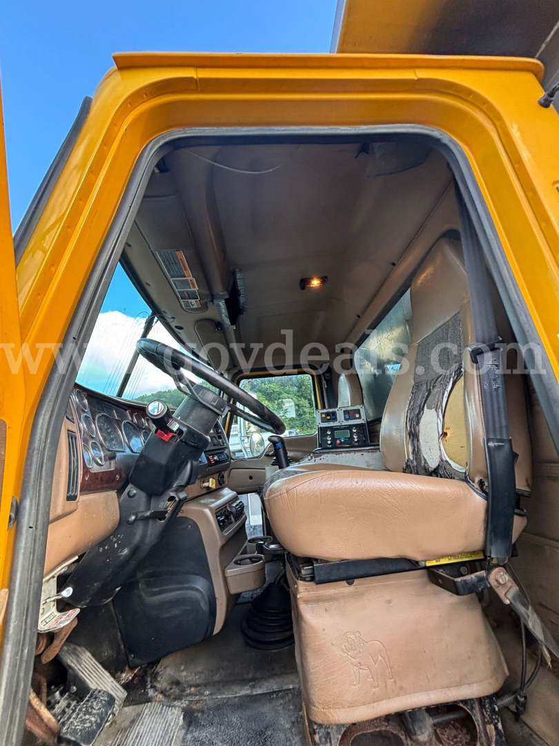 Cab interior of a 2004 Mack CV713 dump truck showing driver seat, steering wheel, and dashboard from open door.