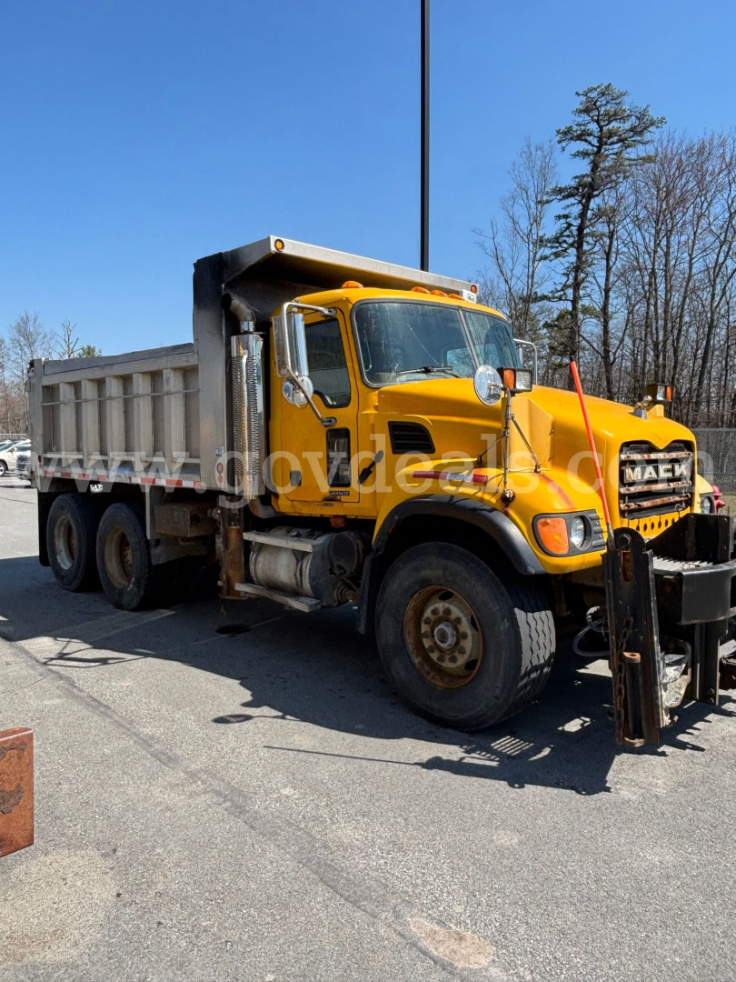 Dump truck: yellow Mack CV713 with a black front grille, dumping bed, large tires, and side mirrors. Visible text includes MA C on grille and DOT information not clearly legible.