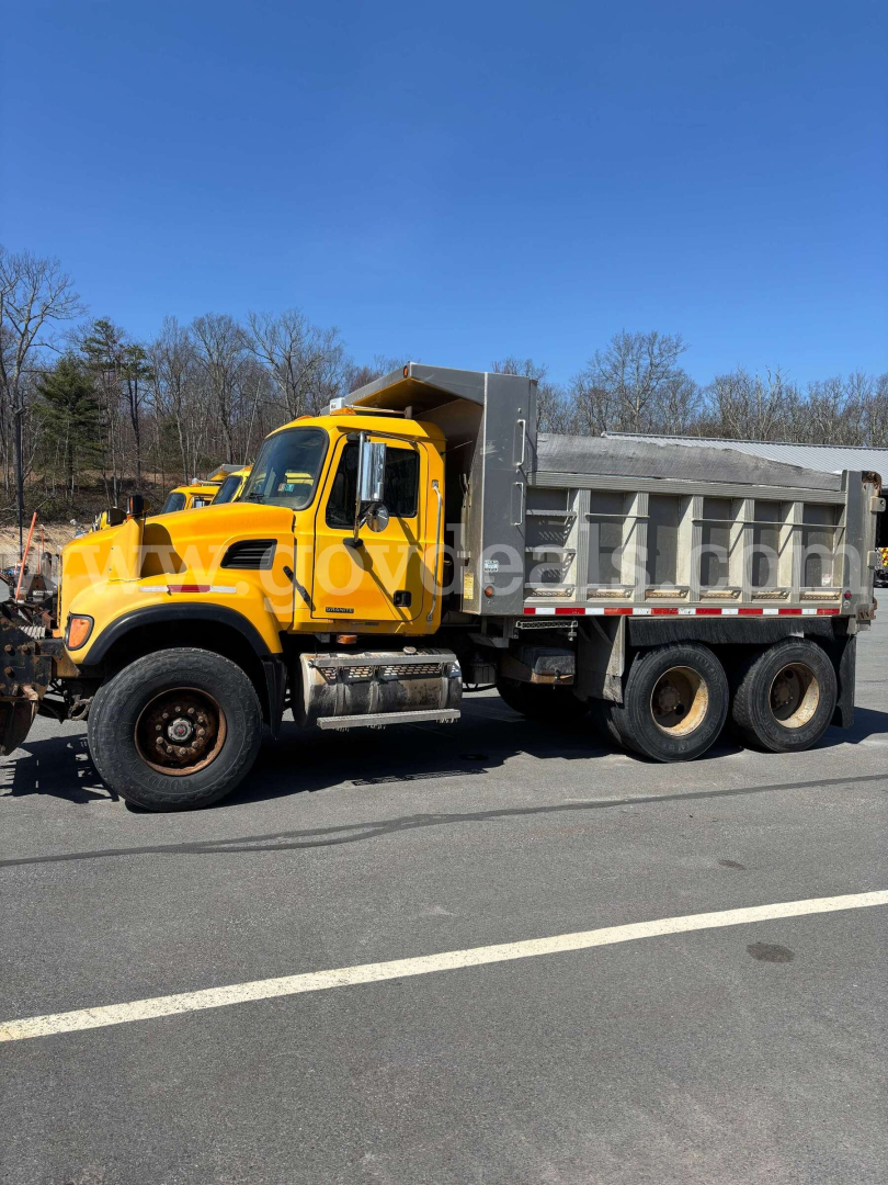 Yellow Mack CV713 dump truck in profile view showing cab, dual rear axles, and metal dump bed.