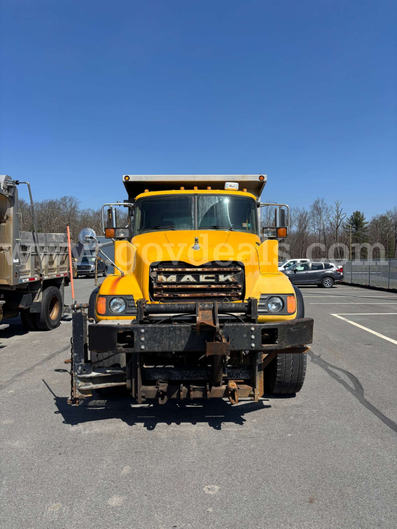 Mack CV713 dump truck front view showing large grille, yellow paint, headlights, and front bumper with hitch.