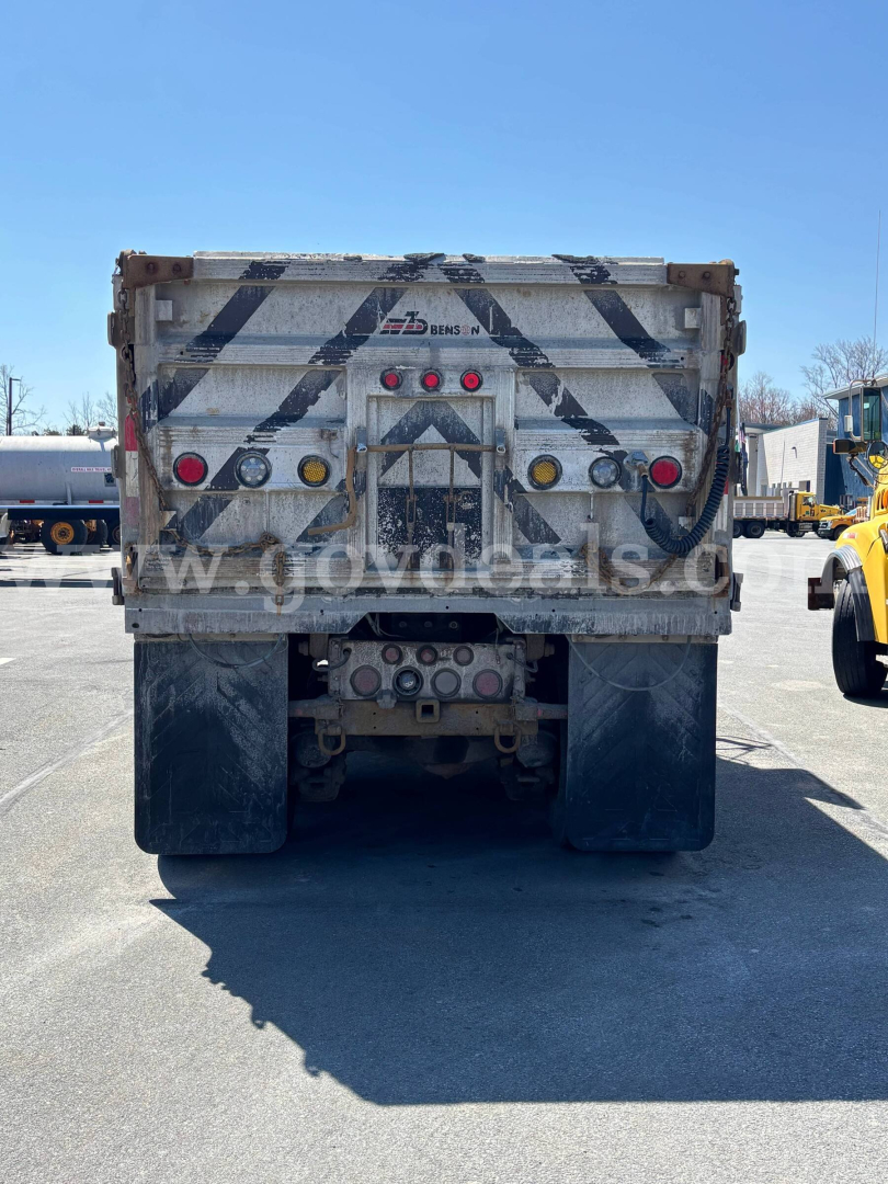 Rear view of a 2004 Mack CV713 dump truck showing tailgate with diagonal black-and-white stripes and red/amber lights, bumper, and hitch area.