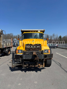 Mack CV713 dump truck front view showing large grille, yellow paint, headlights, and front bumper with hitch.