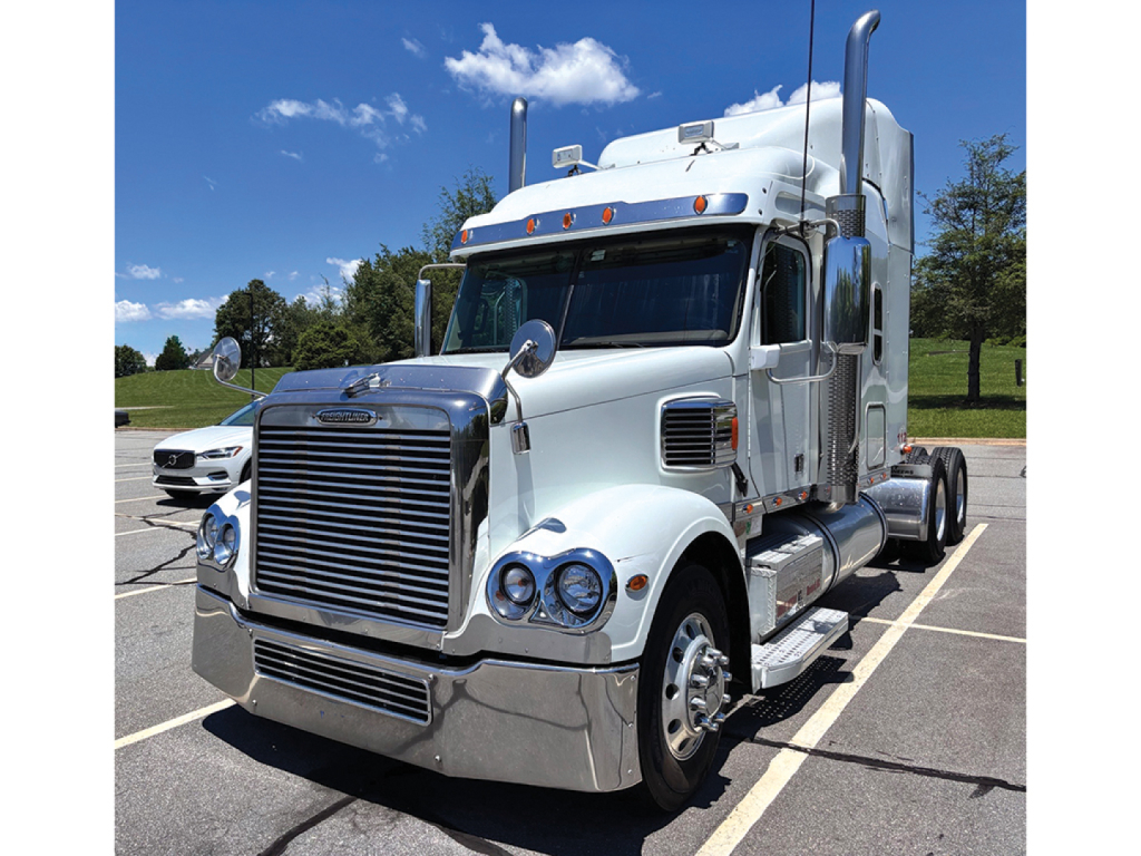 Truck engine bay not visible; Freightliner Coronado tractor with chrome bumper and sleeper cab, front grille, dual exhaust stacks, and polished chrome accents.