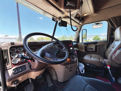 Freightliner Coronado truck cab interior showing dashboard, steering wheel, gauges, driver seat, and passenger seat.
