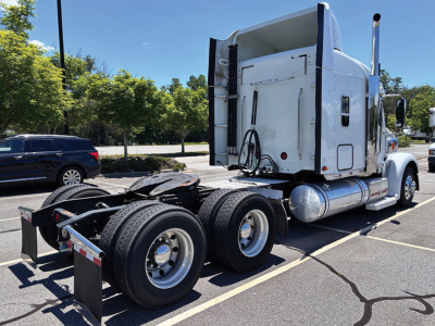 Freightliner Coronado sleeper rigid tractor in a parking lot, rear view shows dual rear axles and mounted fuel tanks with chrome wheels.