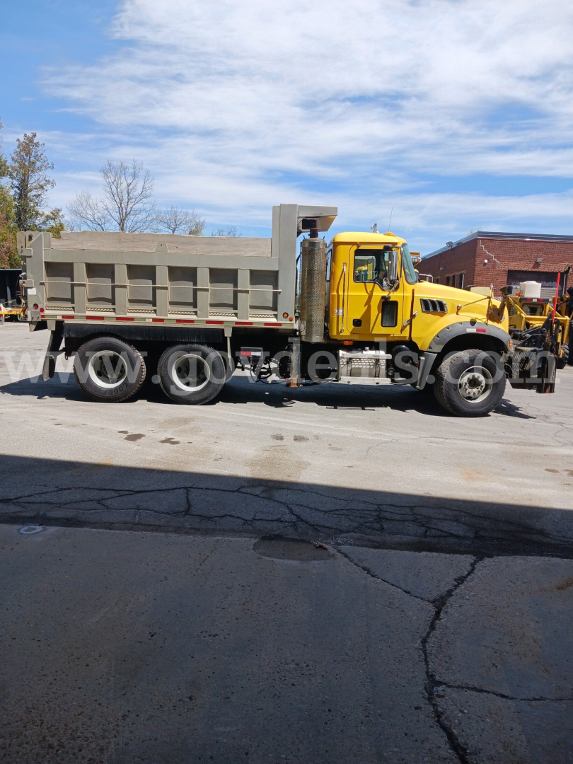 Dump truck side view showing yellow cab and gray dump bed with chrome exhaust and black tires. Visible markings include a watermark across the image; no legible model text is readable.
