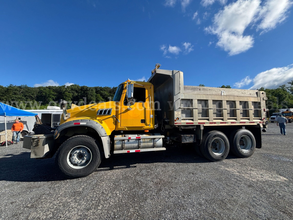 Mack GU713 dump truck side view showing yellow cab and gray dumping bed with suspension and wheels visible.