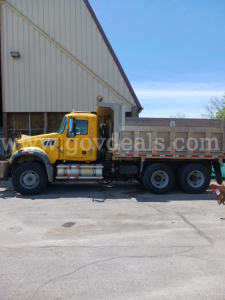 Dump truck side view showing yellow Mack GU713 with dump bed in service configuration.