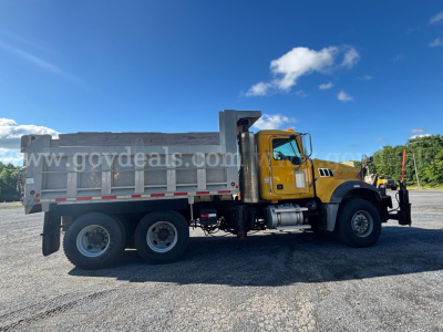 Dump truck side view showing 2009 Mack GU713 dump truck with yellow cab, grey dump bed, aluminum wheels, and side rails.