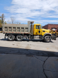 Dump truck side view showing yellow cab and gray dump bed with chrome exhaust and black tires. Visible markings include a watermark across the image; no legible model text is readable.