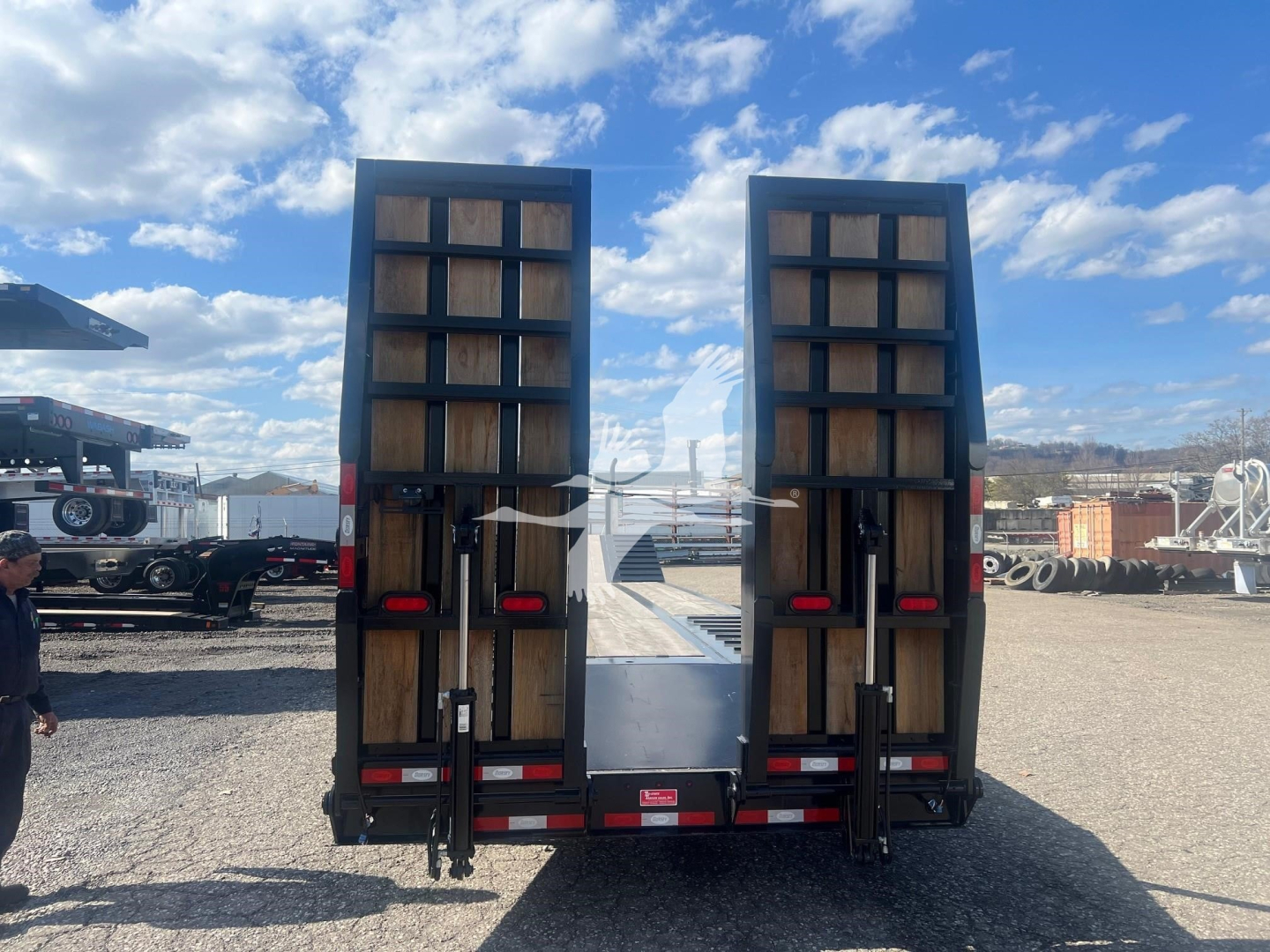 Trailer rear view showing dual hydraulic ramps and stacked wooden deck sections of a Dorsey drop deck trailer.