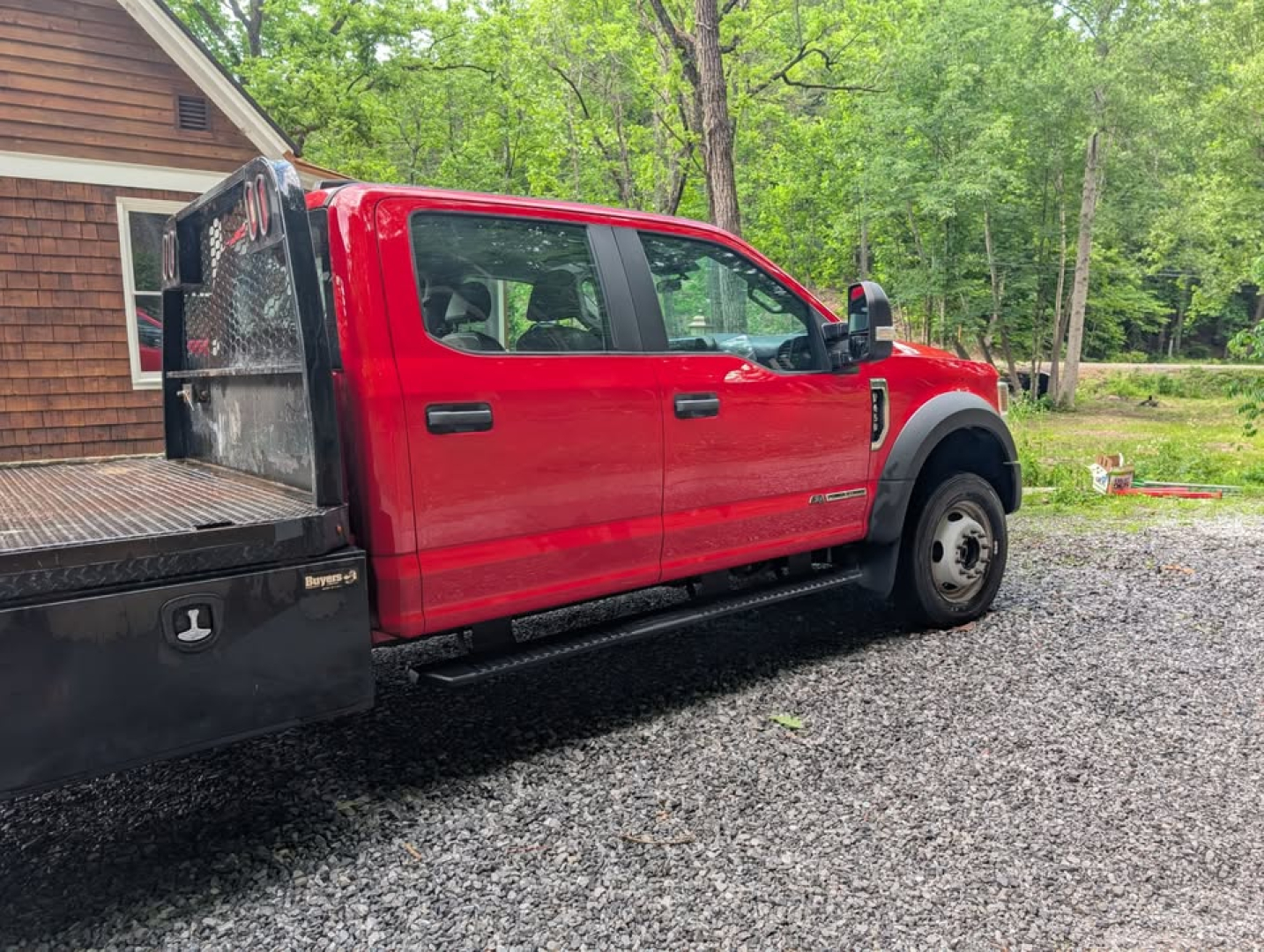 Ford F-450 Super Duty XL utility flatbed truck side view showing red cab and flatbed with diamond plate tool storage in an outdoor lot.
