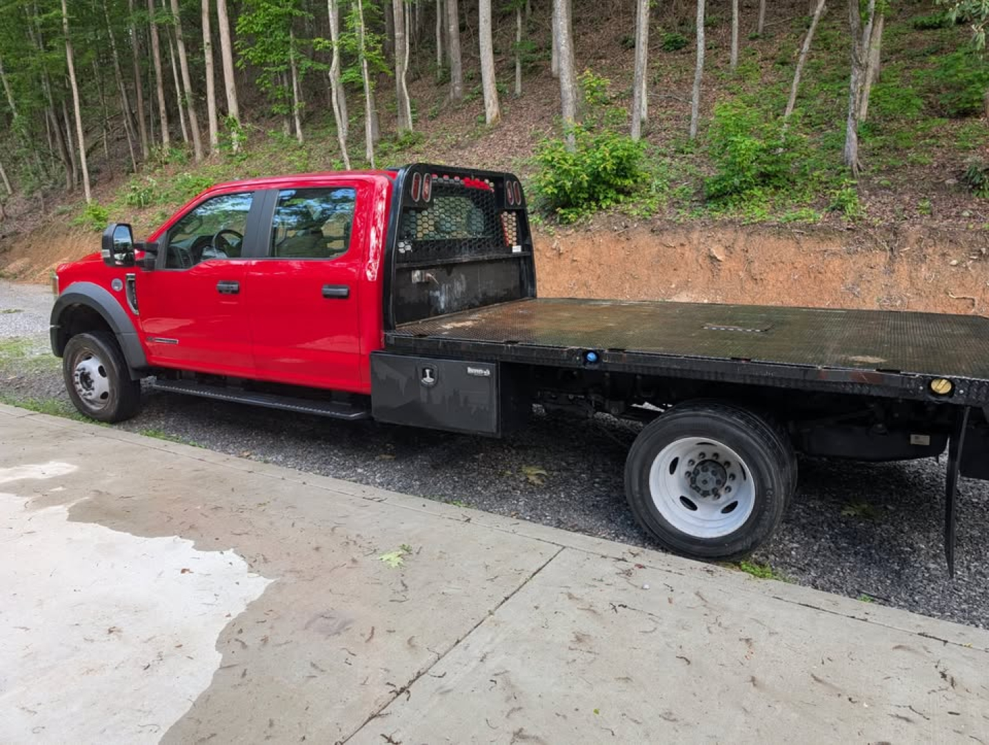 Red 2022 Ford F-450 Super Duty XL pickup with flatbed, side view showing extended cab and flatbed ramp area.