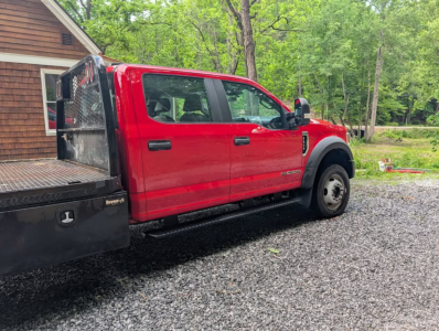 Ford F-450 Super Duty XL utility flatbed truck side view showing red cab and flatbed with diamond plate tool storage in an outdoor lot.