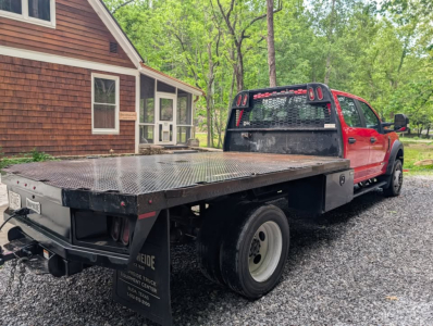 Flatbed tow truck: 2022 Ford F-450 Super Duty XL in a red cab on a black flatbed, dual rear wheels, bumper hitch, utility accents visible.
