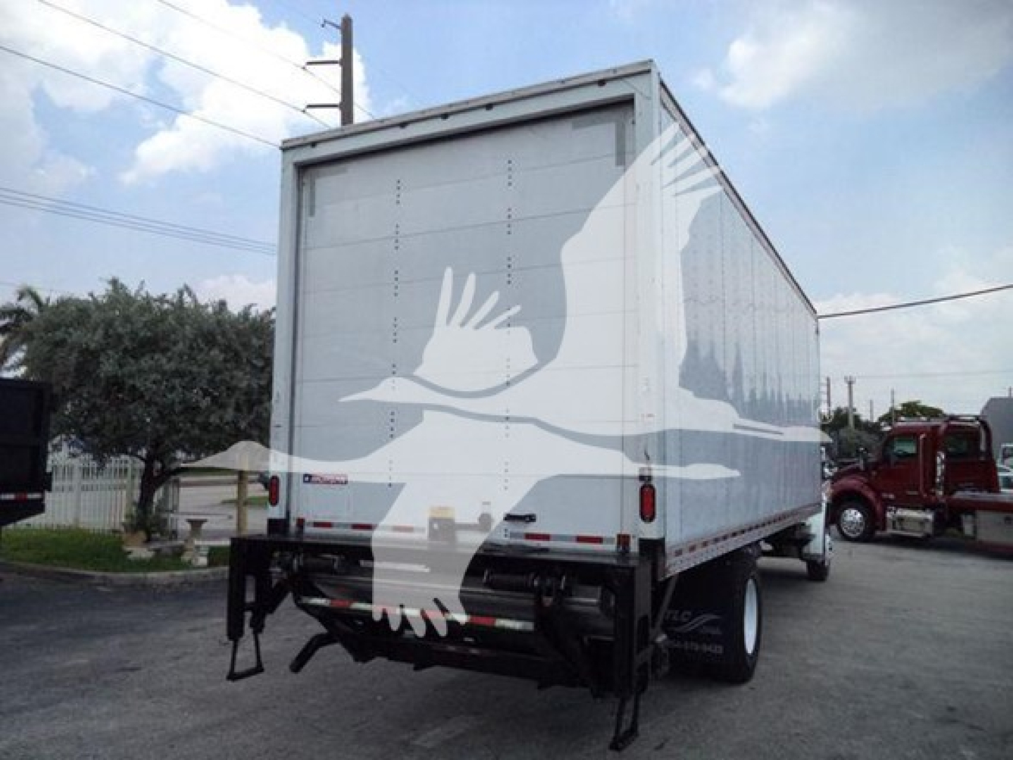 Box truck rear view showing Freightliner M2 106 cargo area with white box and graphic of birds; hydraulic lift gates and rear bumper visible.