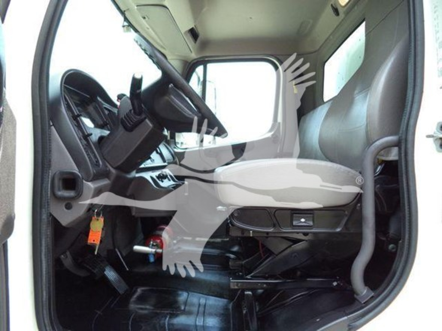 Cab interior of a Freightliner M2 106 truck showing driver seat, steering wheel, pedals, and dashboard from open door.