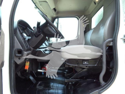 Cab interior of a Freightliner M2 106 truck showing driver seat, steering wheel, pedals, and dashboard from open door.