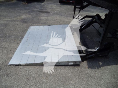 Flatbed pallet or ramp with light gray surface and black mechanical components visible in background.