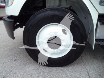 Wheel of a Freightliner M2 106 truck showing a large black tire and white steel wheel with hub and lug nuts; partial fender and bodywork visible.