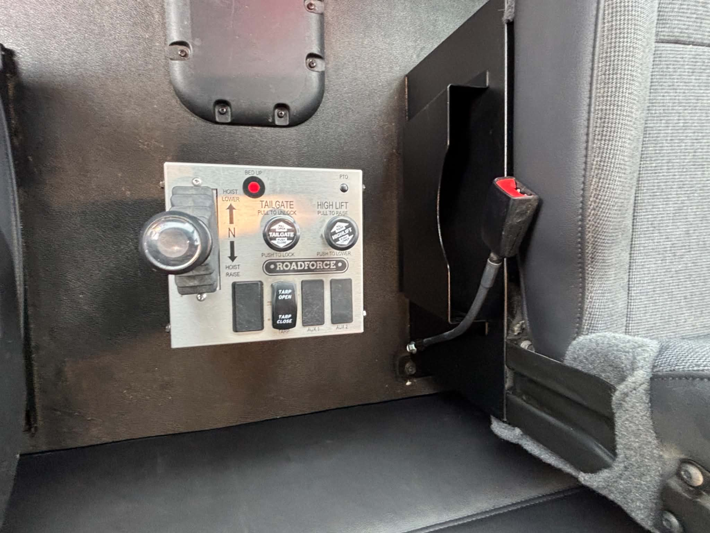 Kenworth T880 interior console panel showing control switches and gauges, including a small round knob and a rectangular control panel with labels like UP, DOWN, and ROAD FORCED. Some text visible: THROTTLE? HANDLE? and multiple black push-