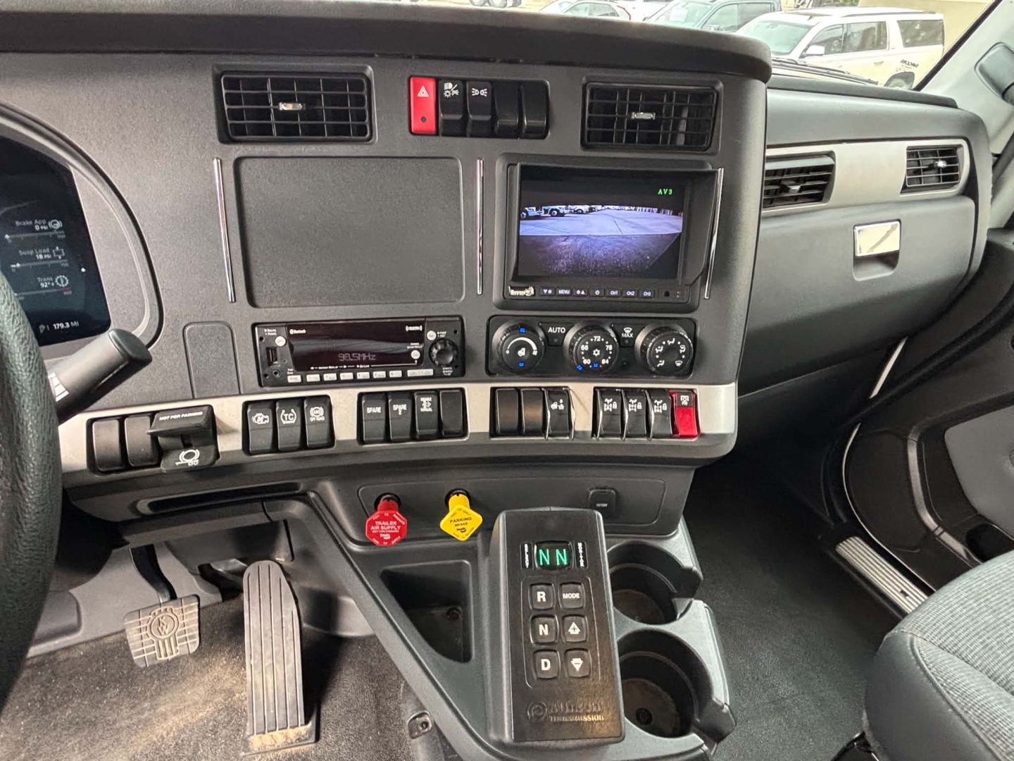 Kenworth T880 dash area showing center console with climate controls, radio, small monitor, and gear shifter column; various toggles and red hazard switch visible.
