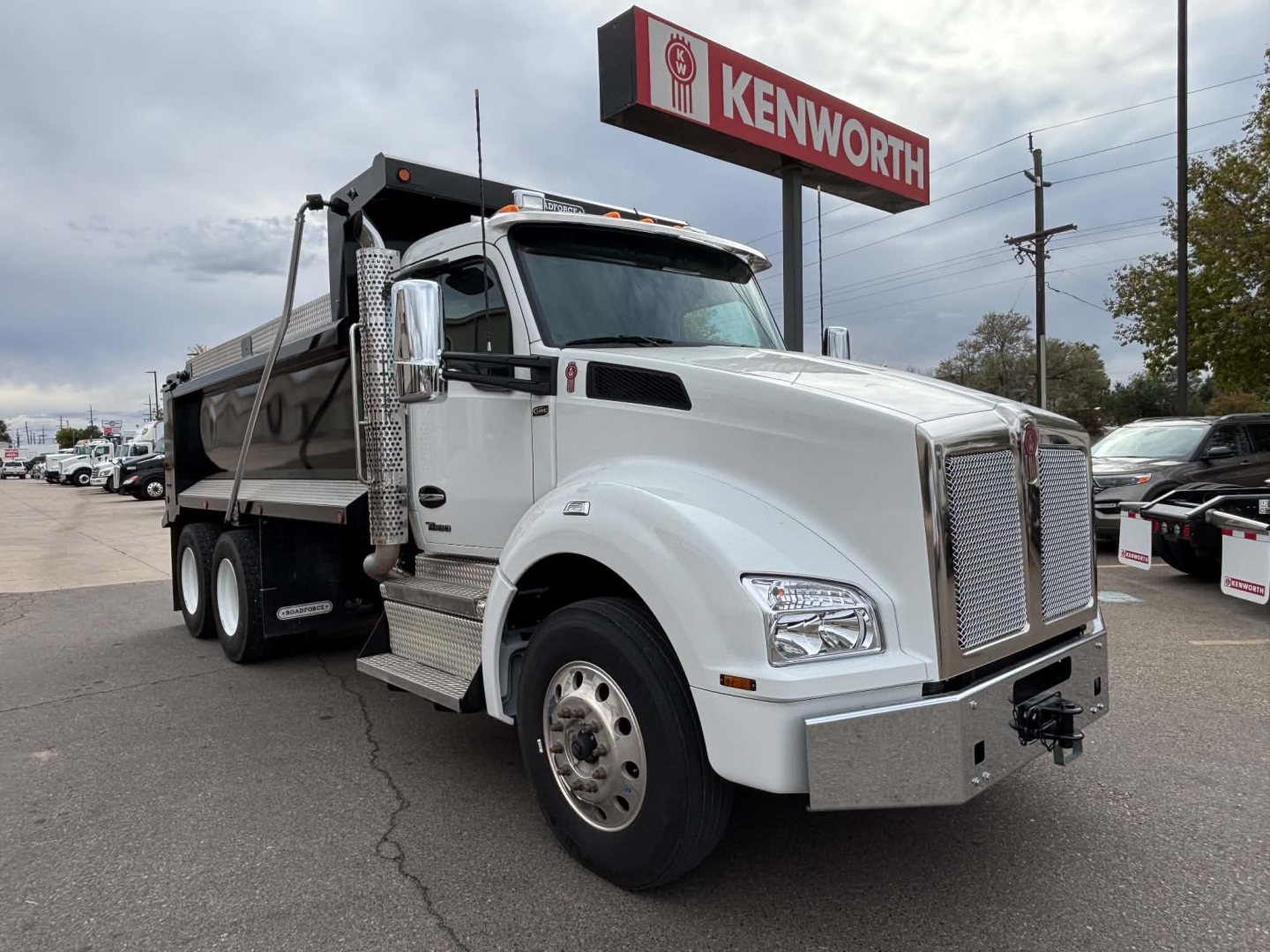 Kenworth T880 dump truck in service bay showing front grille, large chrome bumper, side exhaust, and dump bed under clear sky.