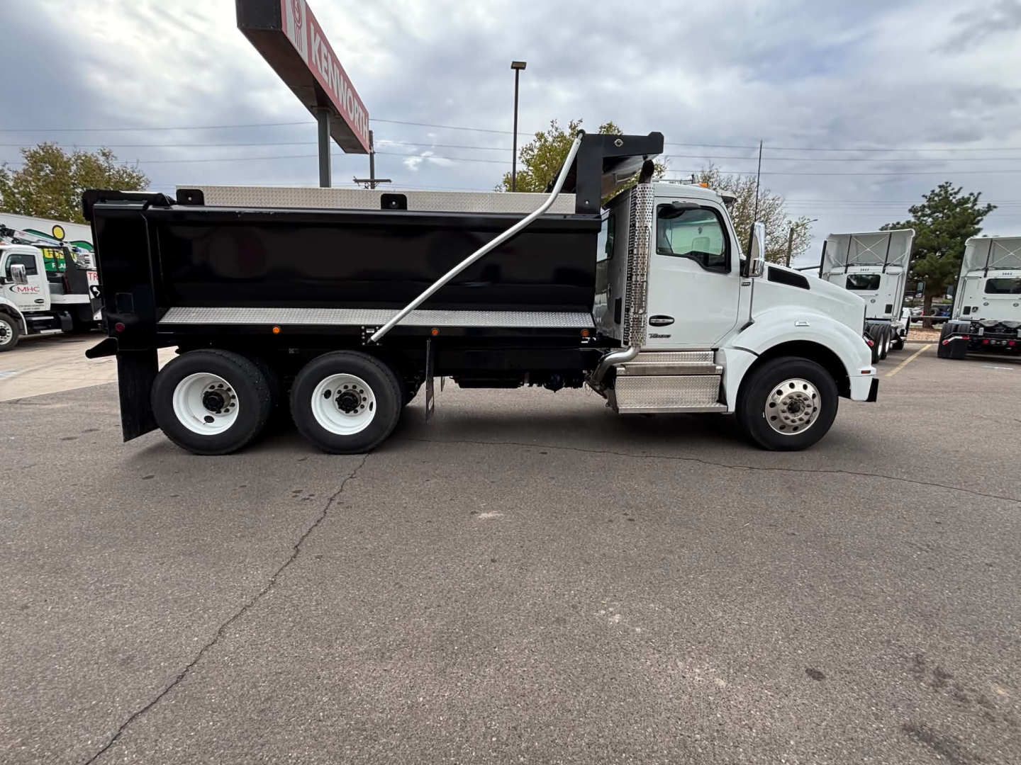 Kenworth T880 dump truck side view showing front cab and black dump bed with chrome steps and Silver aluminum side rails.