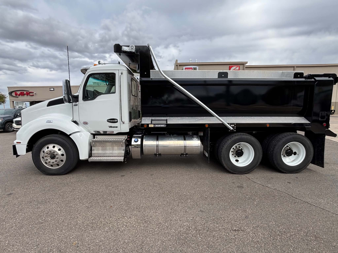 Kenworth T880 dump truck side view showing black dump body, white cab, chrome fuel tanks, dual rear axles, and front axle with wheel.