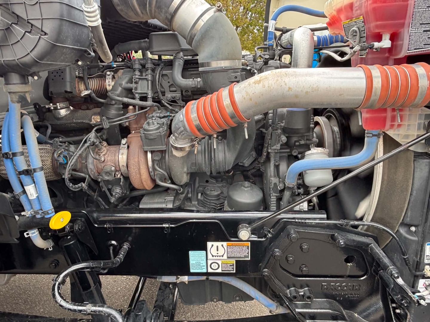 Kenworth T880 engine bay with intercooler hoses, turbocharger, and coolant lines visible in a dump truck, side view showing engine components.