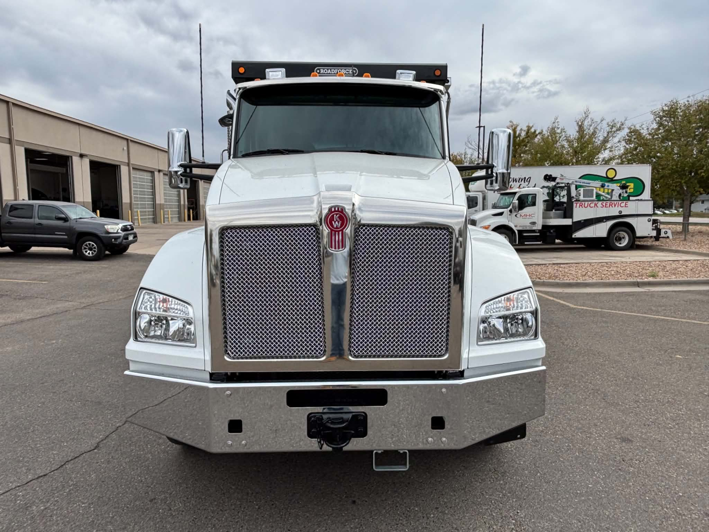Kenworth T880 front view showing large chrome grille, bumper, and headlights. Silver truck with chrome mirrors and center Kenworth emblem.